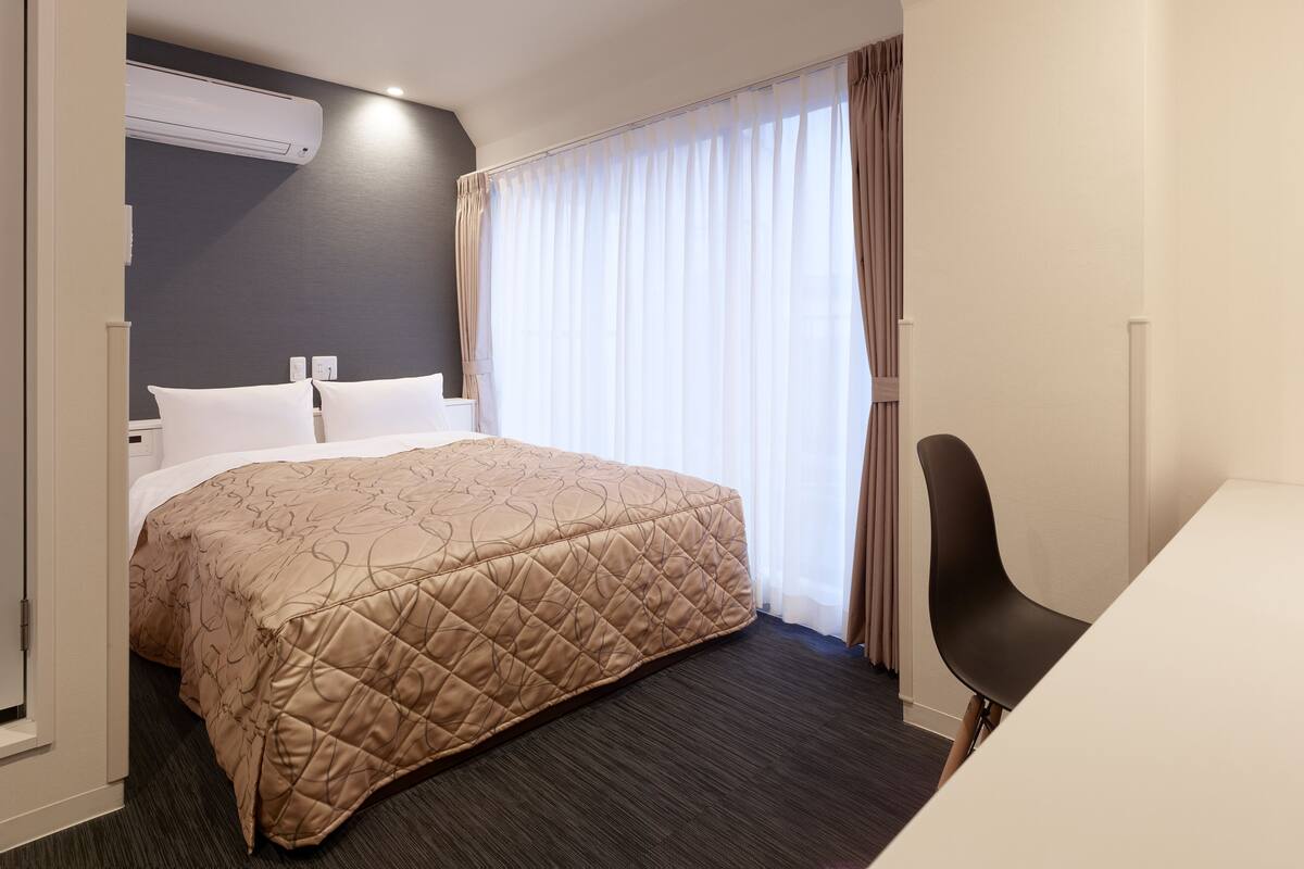 A hotel room with a bed, a desk, and a window with curtains.