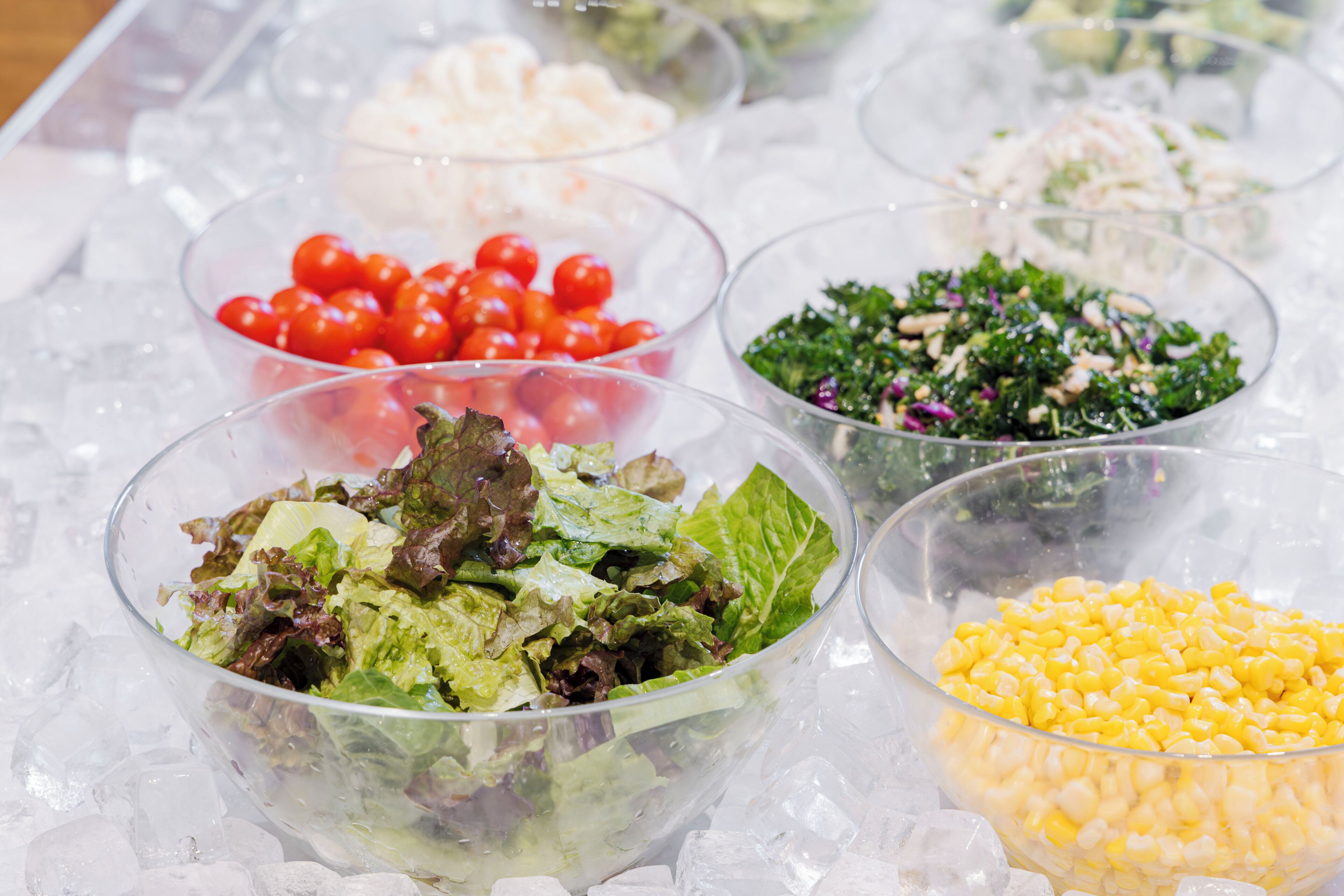 A variety of food bowls on ice, including salads and corn.