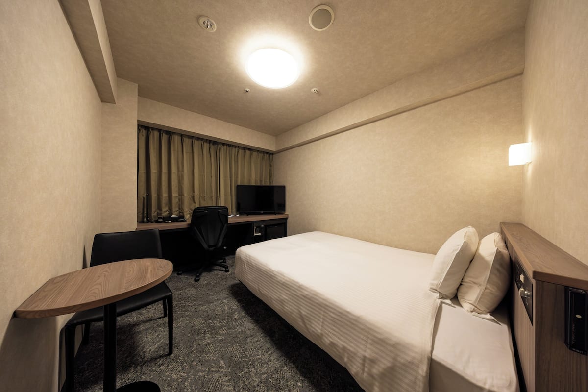 Ein Hotelzimmer mit Bett, Schreibtisch, Stuhl, Fernseher und einem kleinen Tisch.