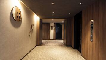 A hotel hallway with a wooden wall, a carpeted floor, a round wall clock, and an elevator.