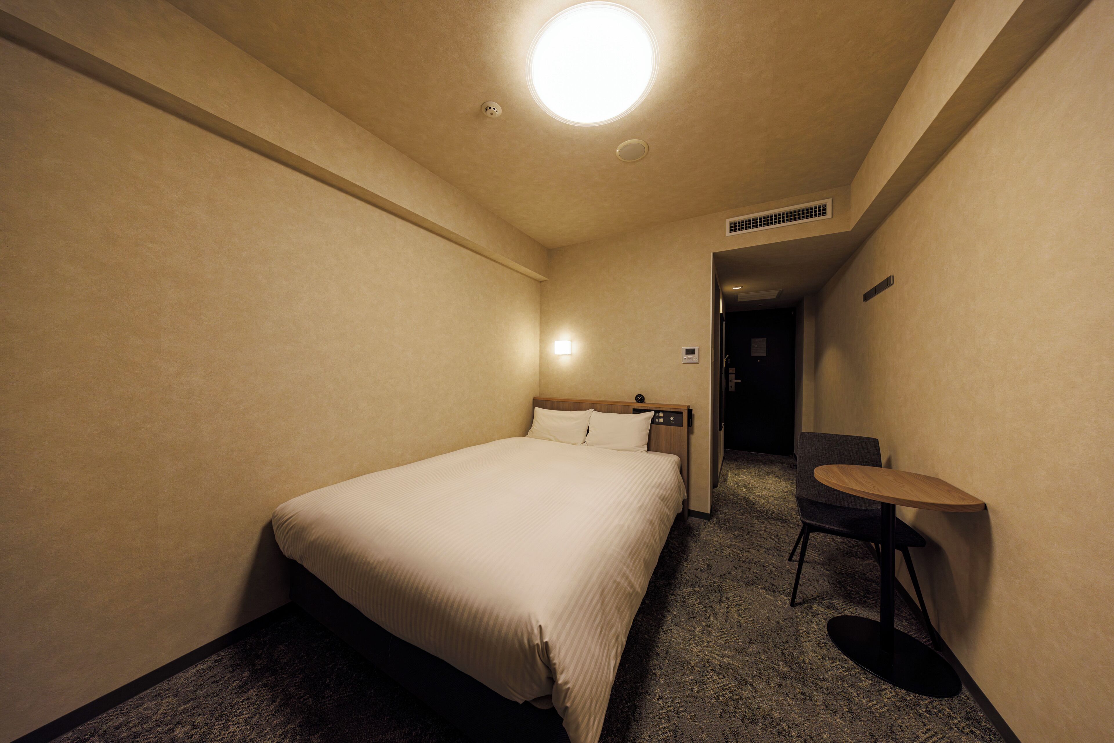 A hotel room with a bed, a small table, and a chair.