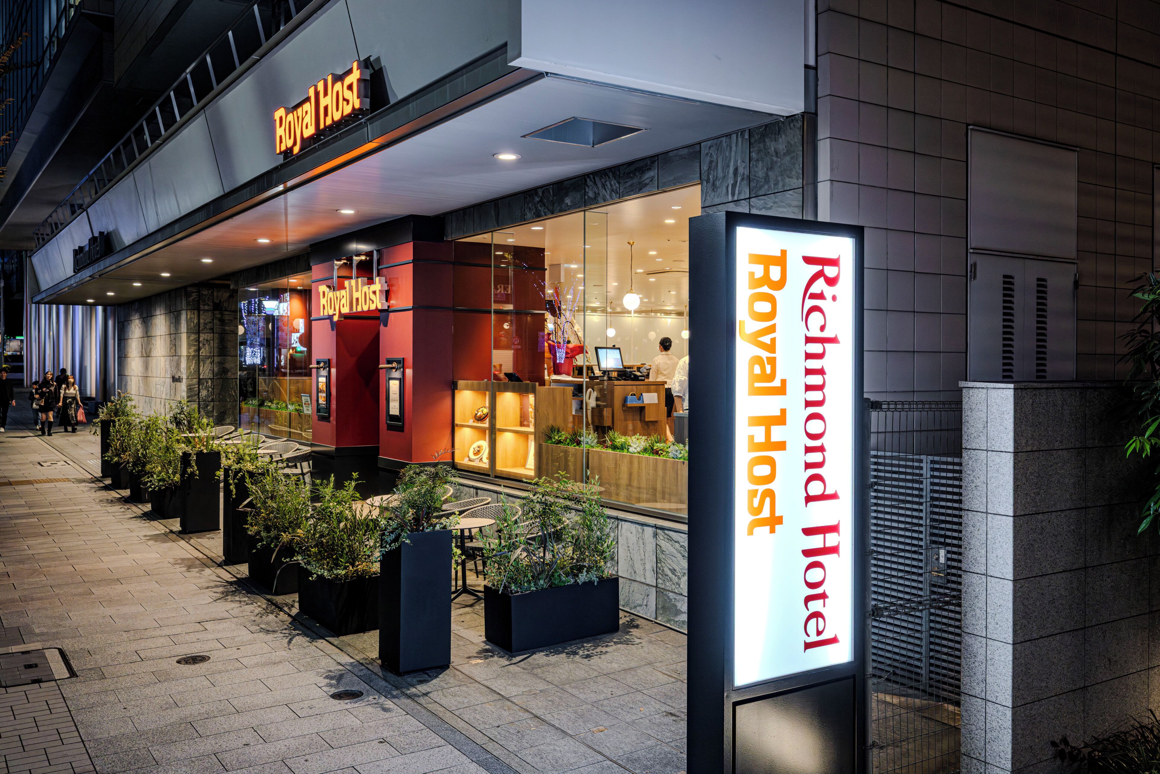 A hotel entrance with a sign for 'Richmond Hotel Royal Host' and a visible outdoor seating area with potted plants.