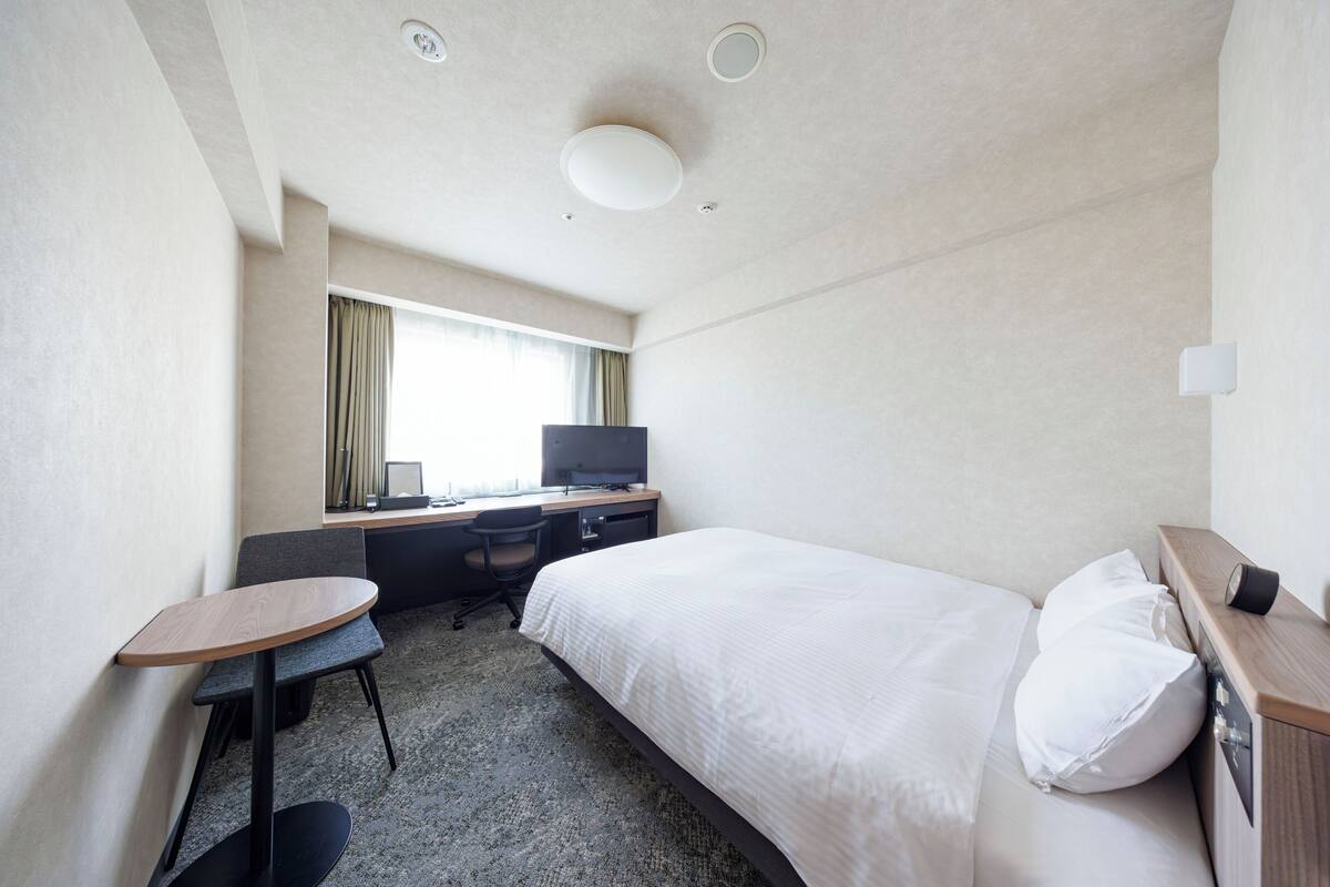 Ein Hotelzimmer mit einem Bett, einem Schreibtisch mit Stuhl, einem Fernseher und einem kleinen Tisch.