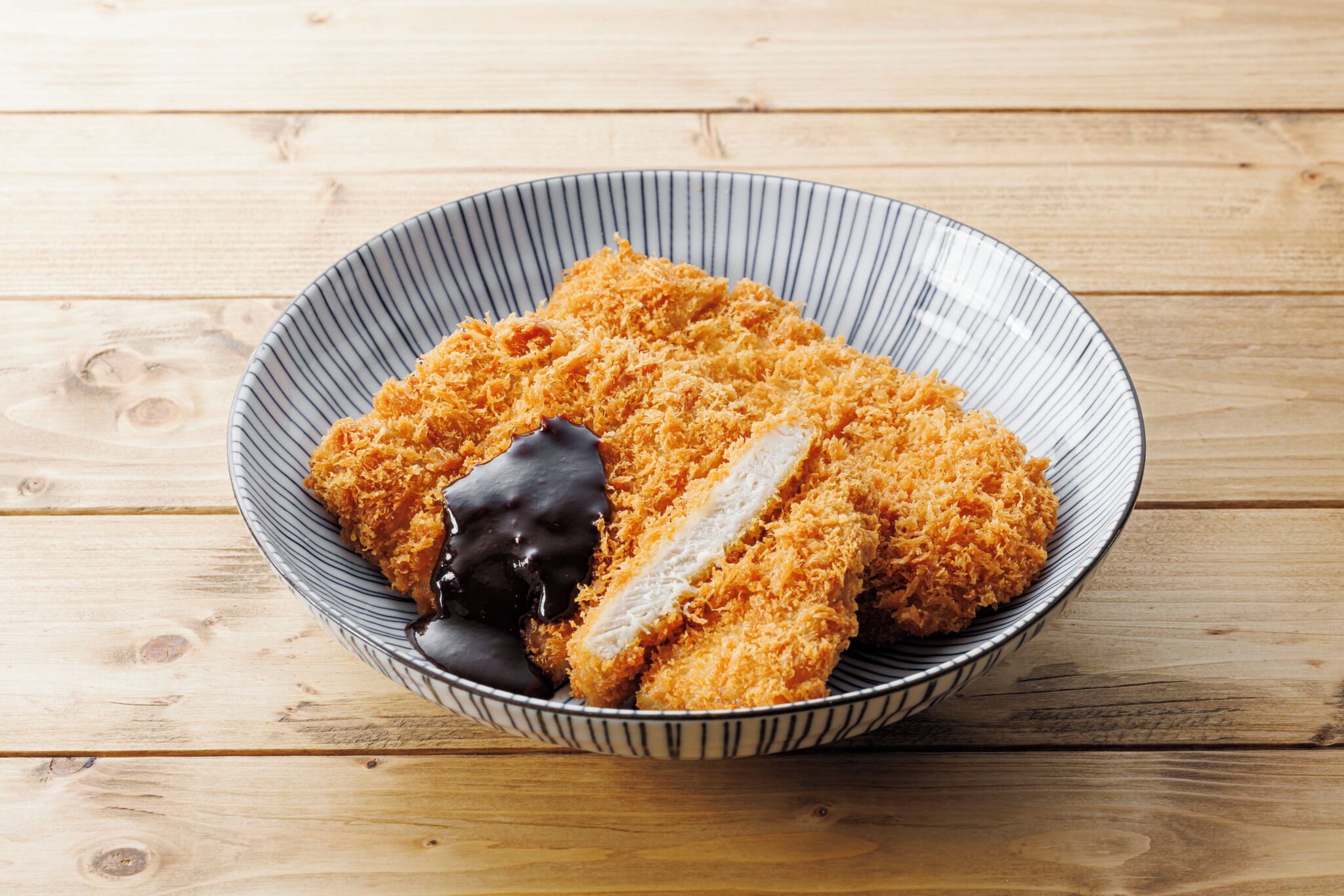 A bowl of breaded and fried food with a chocolate topping on a wooden table.