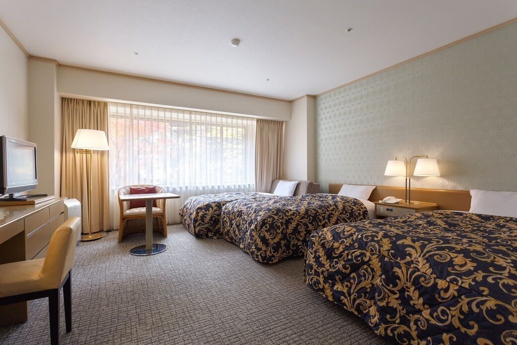 A hotel room with two beds, a desk, a chair, a TV, and a window with curtains.