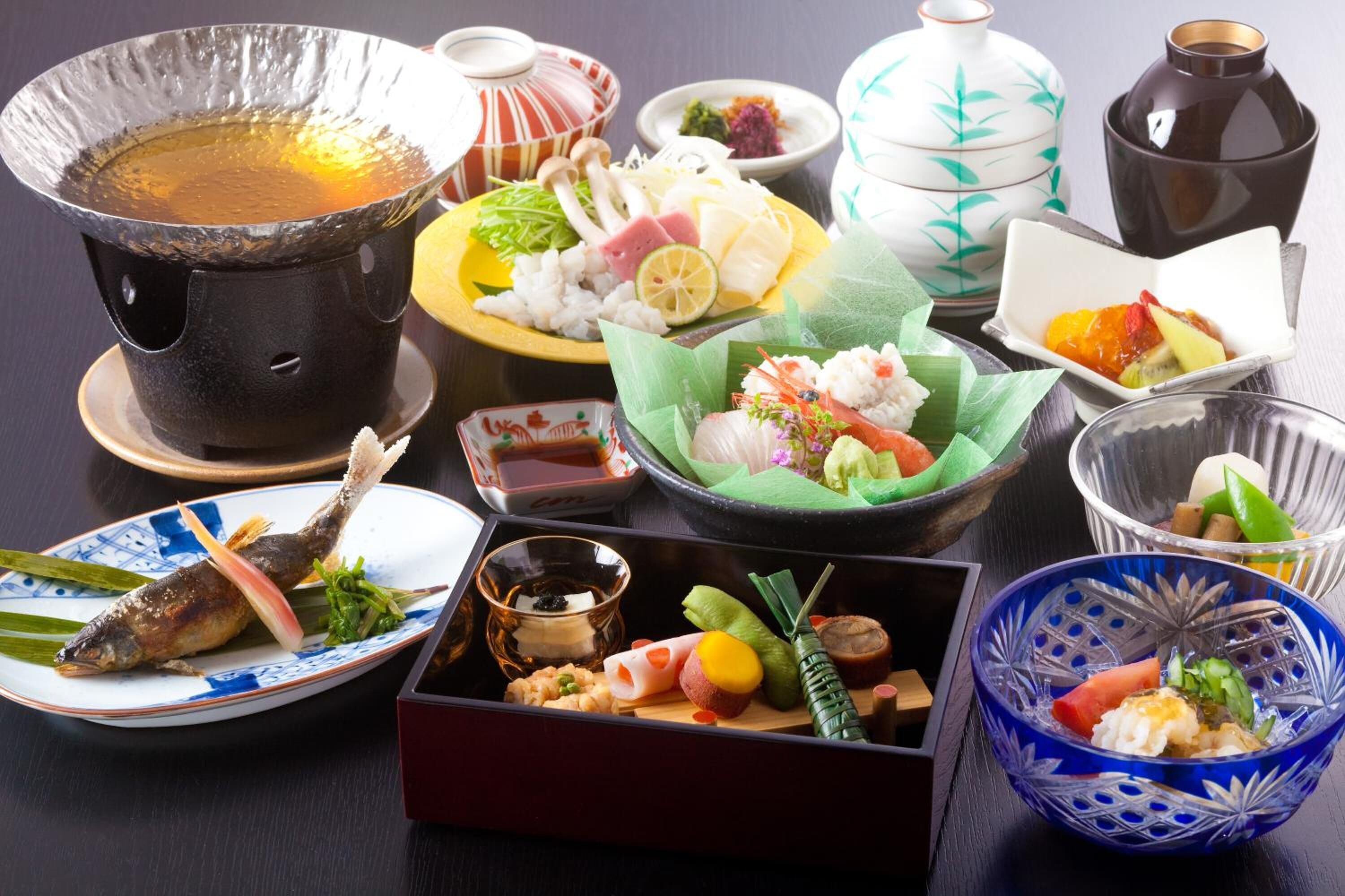 A variety of Japanese dishes, including sushi, sashimi, and a hot pot, arranged on a table.