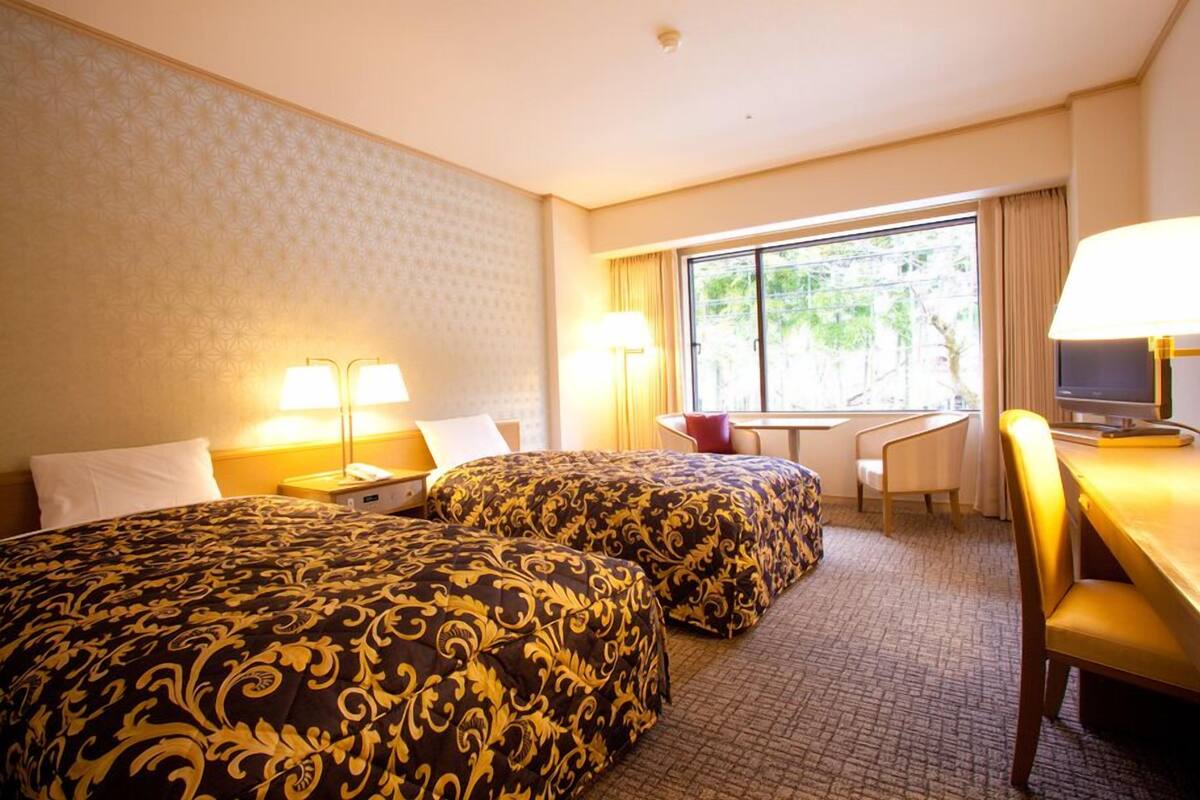 A hotel room with two beds, a desk, a chair, and a TV.
