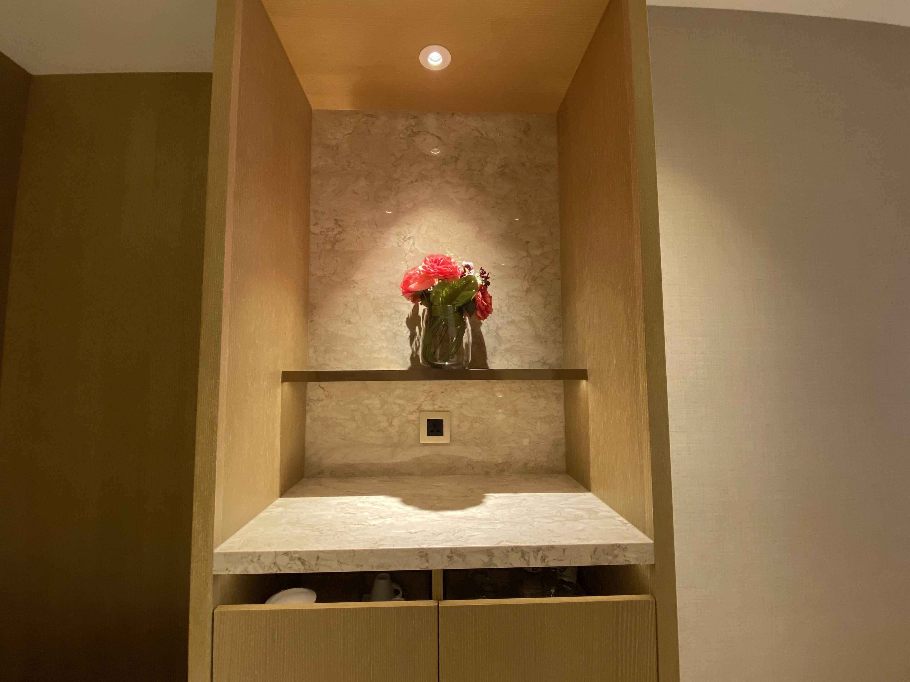 A bathroom with a marble countertop, a wooden cabinet below, and a vase with flowers on a shelf.