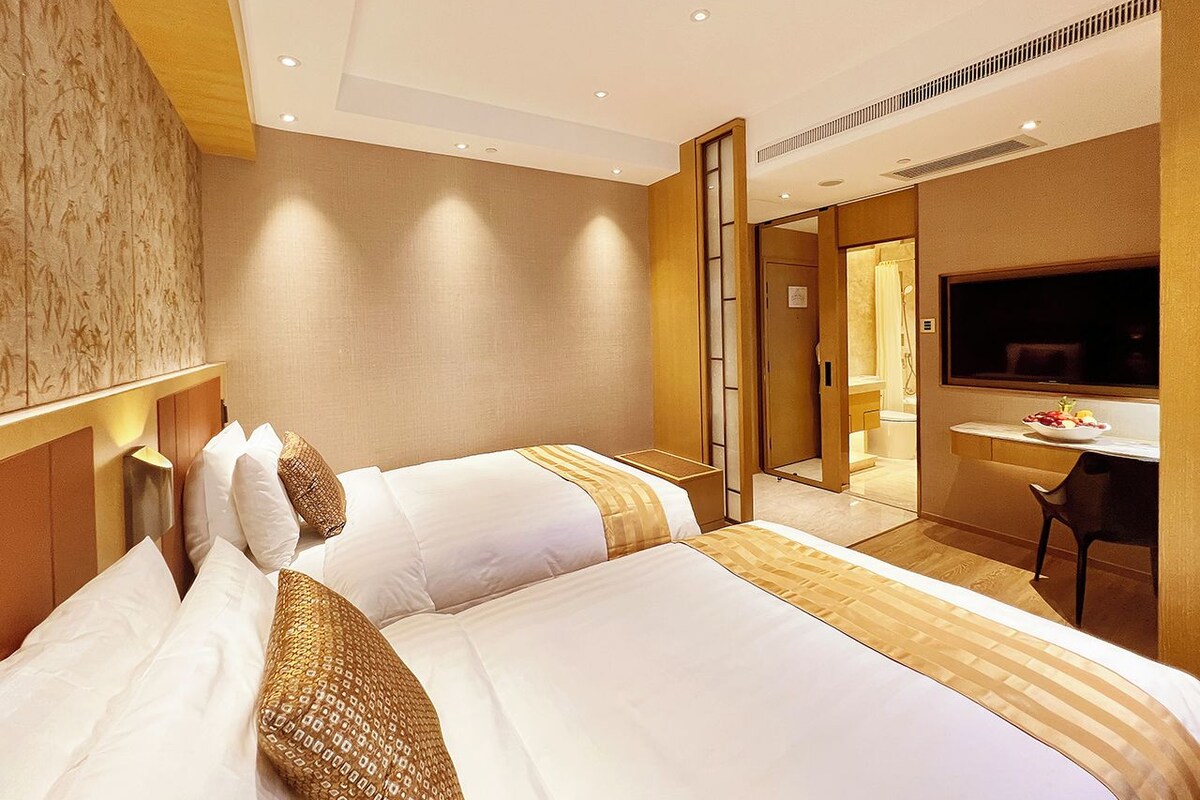 A hotel room with two beds, a desk, and a TV.