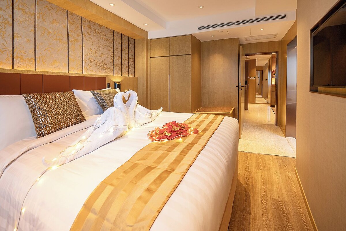 A hotel room with a large bed, a wooden headboard, and a view of the hallway.