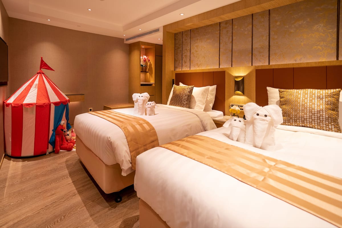 A hotel room with two beds, a red and white striped tent, and plush toys on the floor.