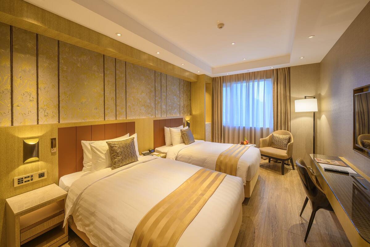 A hotel room with two beds, a desk, a chair, and a large window with curtains.