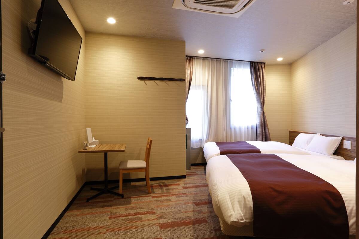 Hotelkamer met twee bedden, een bureau, een stoel, een televisie en een raam met gordijnen.