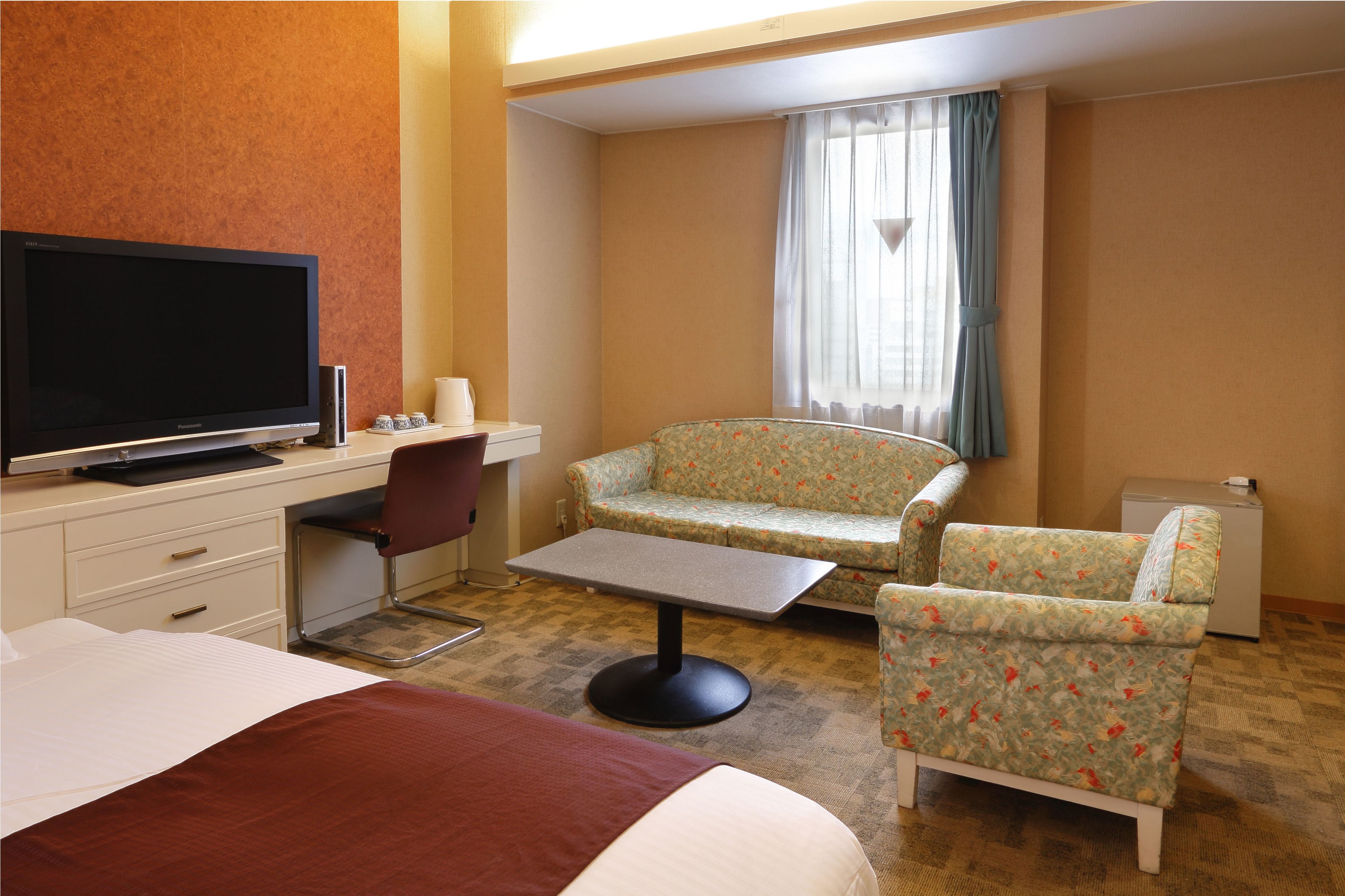 A hotel room with a bed, a desk, a television, a chair, and a sofa.