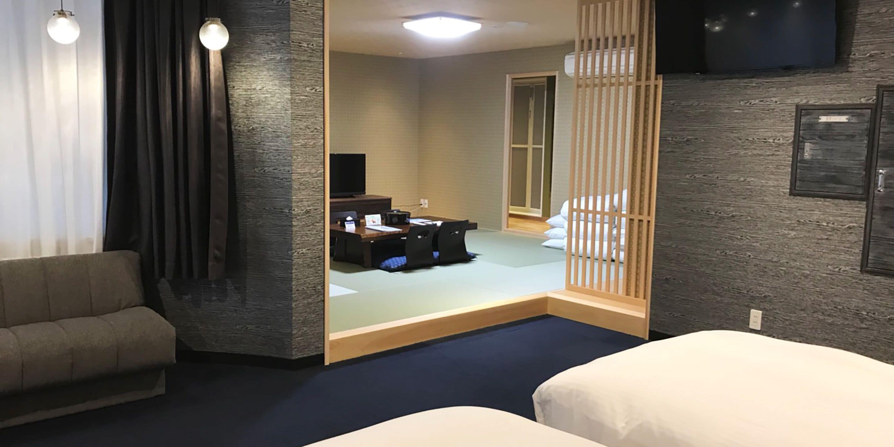 A hotel room with a sofa, two beds, a desk with a computer, and a TV.