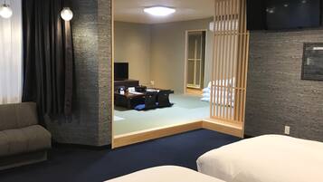 A hotel room with a sofa, two beds, a desk with a computer, and a TV.