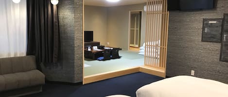 A hotel room with a sofa, two beds, a desk with a computer, and a TV.