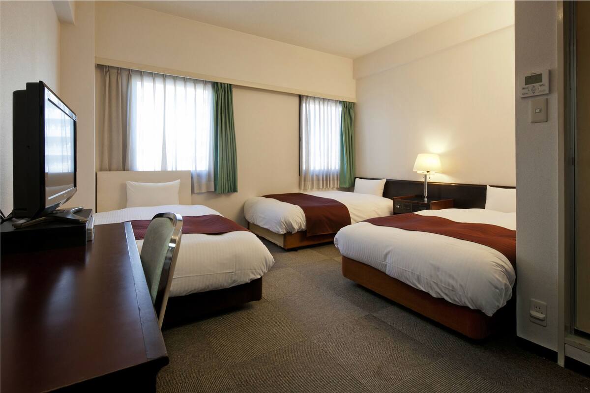 Een hotelkamer met drie bedden, een bureau, een televisie en een lamp.