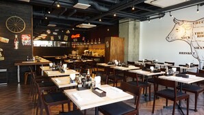 A restaurant with multiple tables and chairs, a counter with a menu, and a wall with a cow illustration.