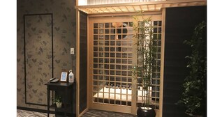A traditional Japanese room with tatami flooring, a sliding door with a grid pattern, a small table with a framed picture and bottles, and a potted plant.