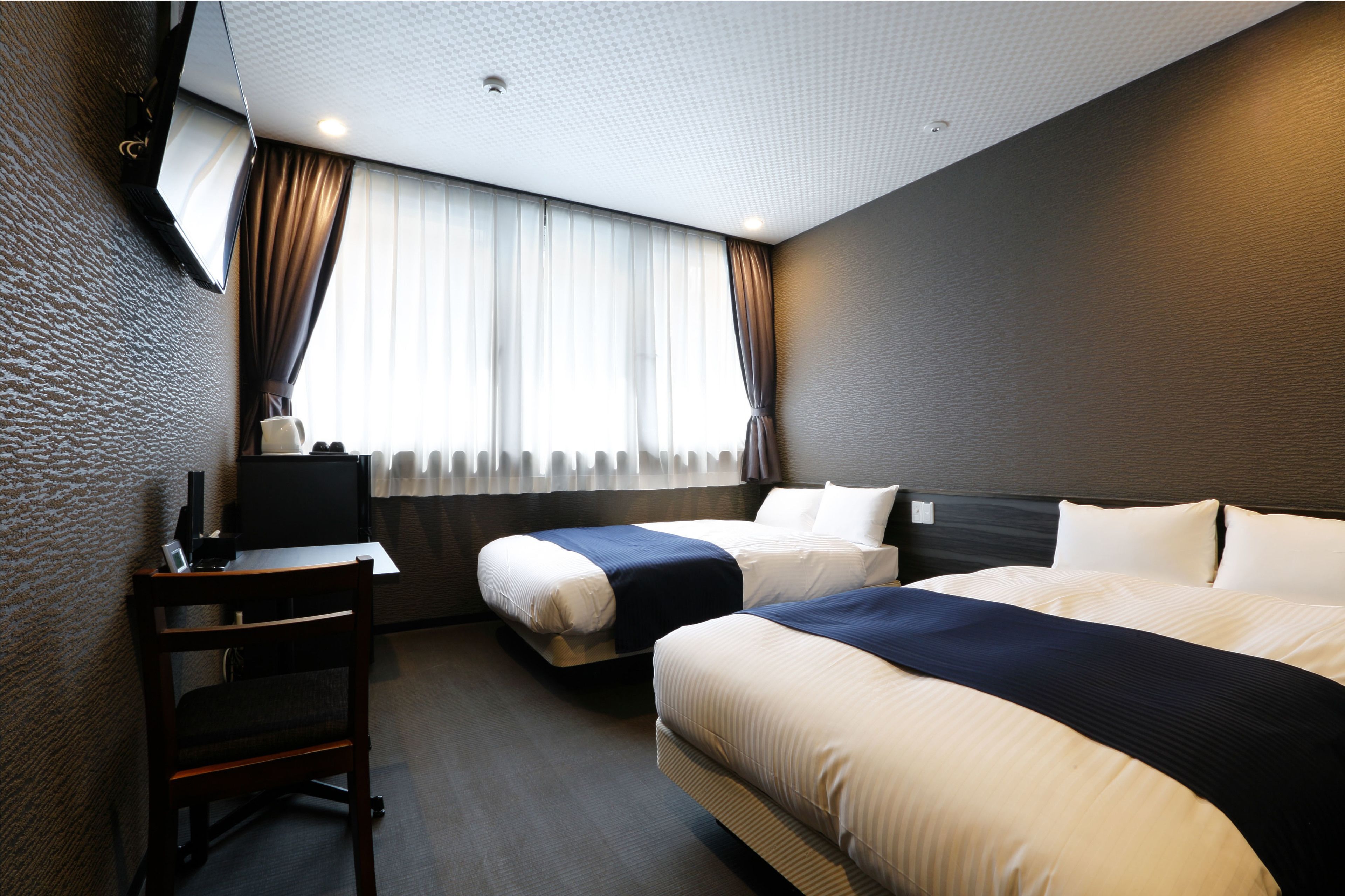 A hotel room with two beds, a desk, a chair, and a television.