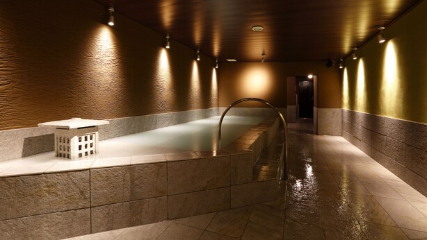 A spa area with a large bathtub, a small seating area, and a wooden ceiling.