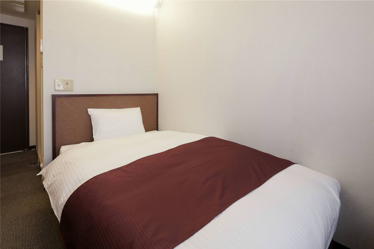 Een hotelkamer met een eenpersoonsbed, een hoofdbord en een tapijtvloer.