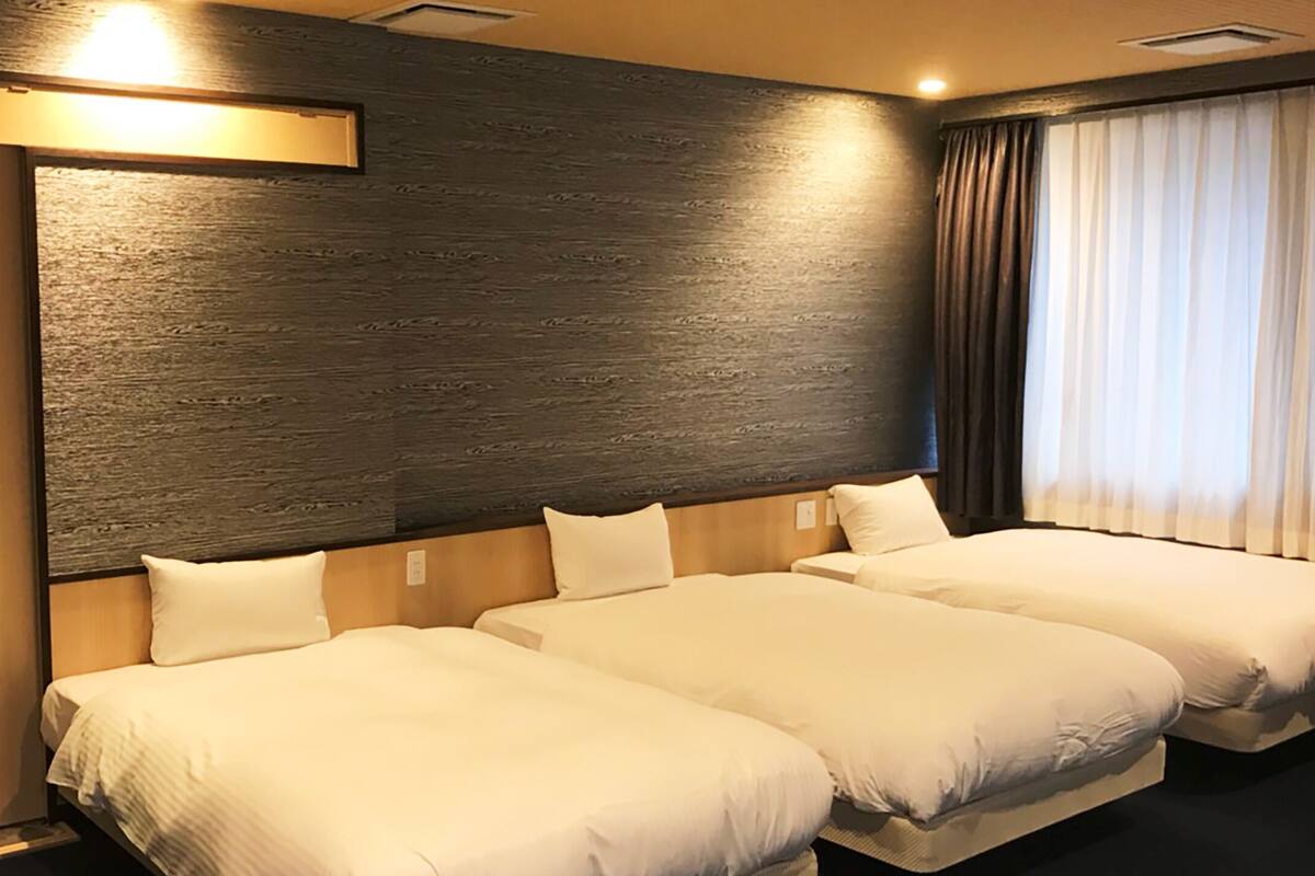 Een hotelkamer met twee bedden, een hoofdbord van donker hout en een groot raam met gordijnen.