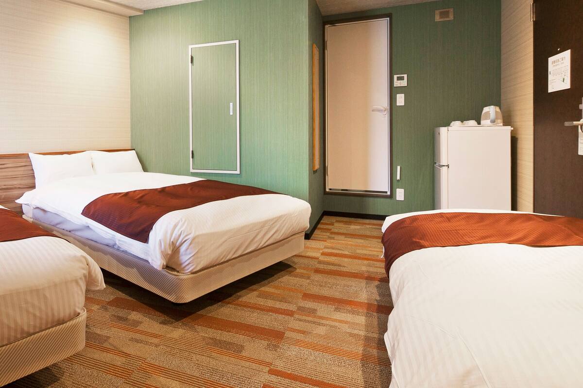 Een hotelkamer met drie bedden, een koelkast en een deur met een spiegel.