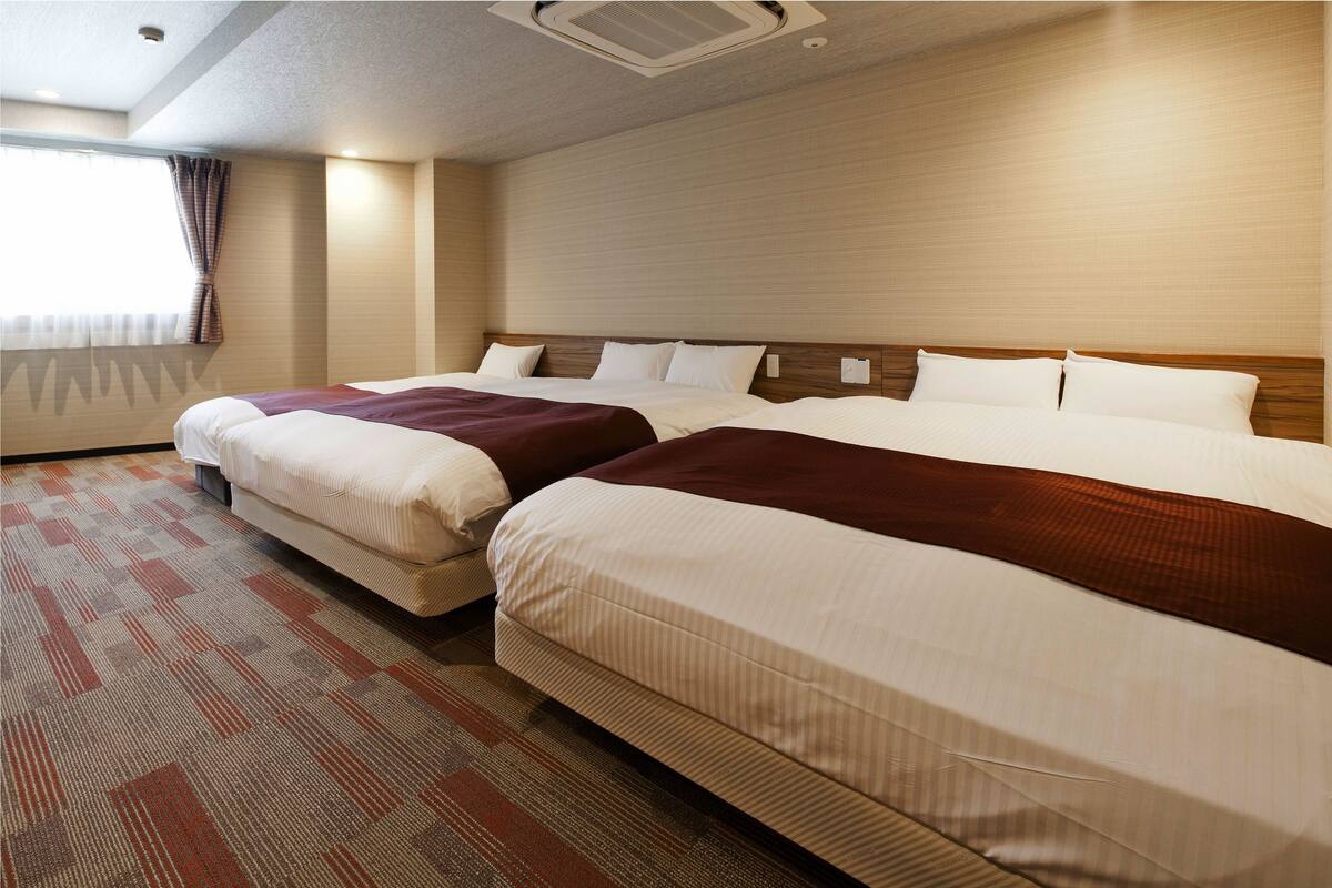 Een hotelkamer met twee bedden, een groot raam met gordijnen en een kamerbreed tapijt met dessin.