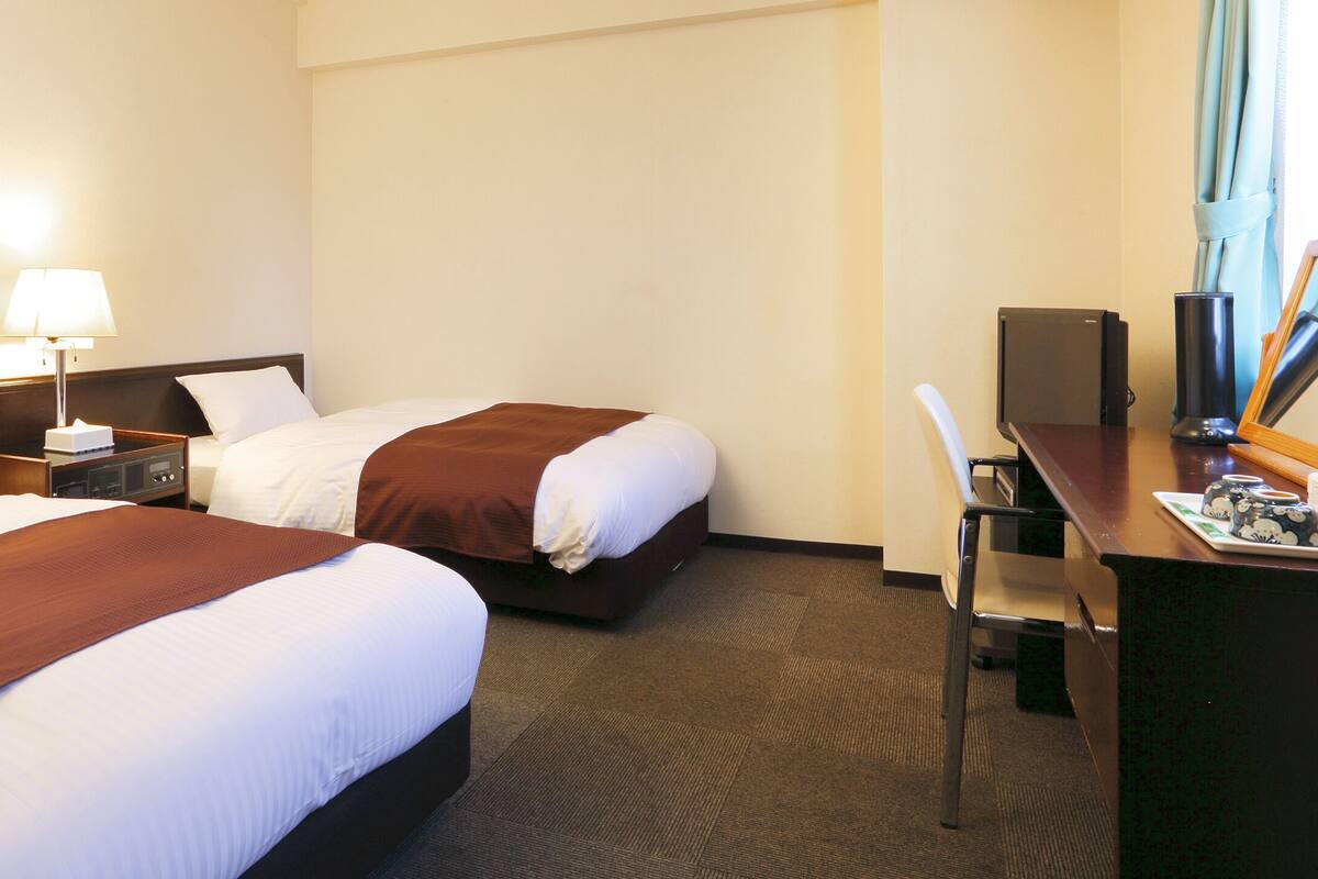 Een hotelkamer met twee bedden, een bureau met een computer, een lamp en een stoel.