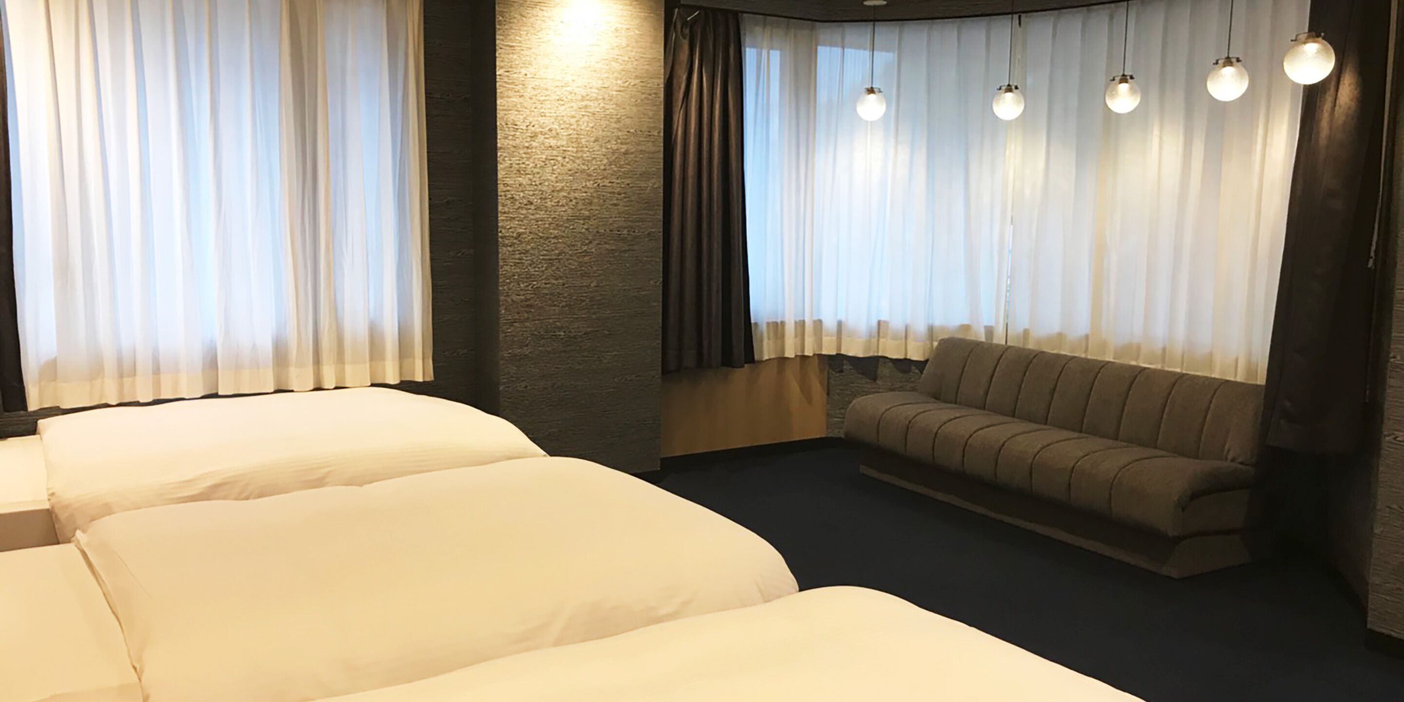 Quarto de hotel com três camas, um sofá e uma janela grande com cortinas.