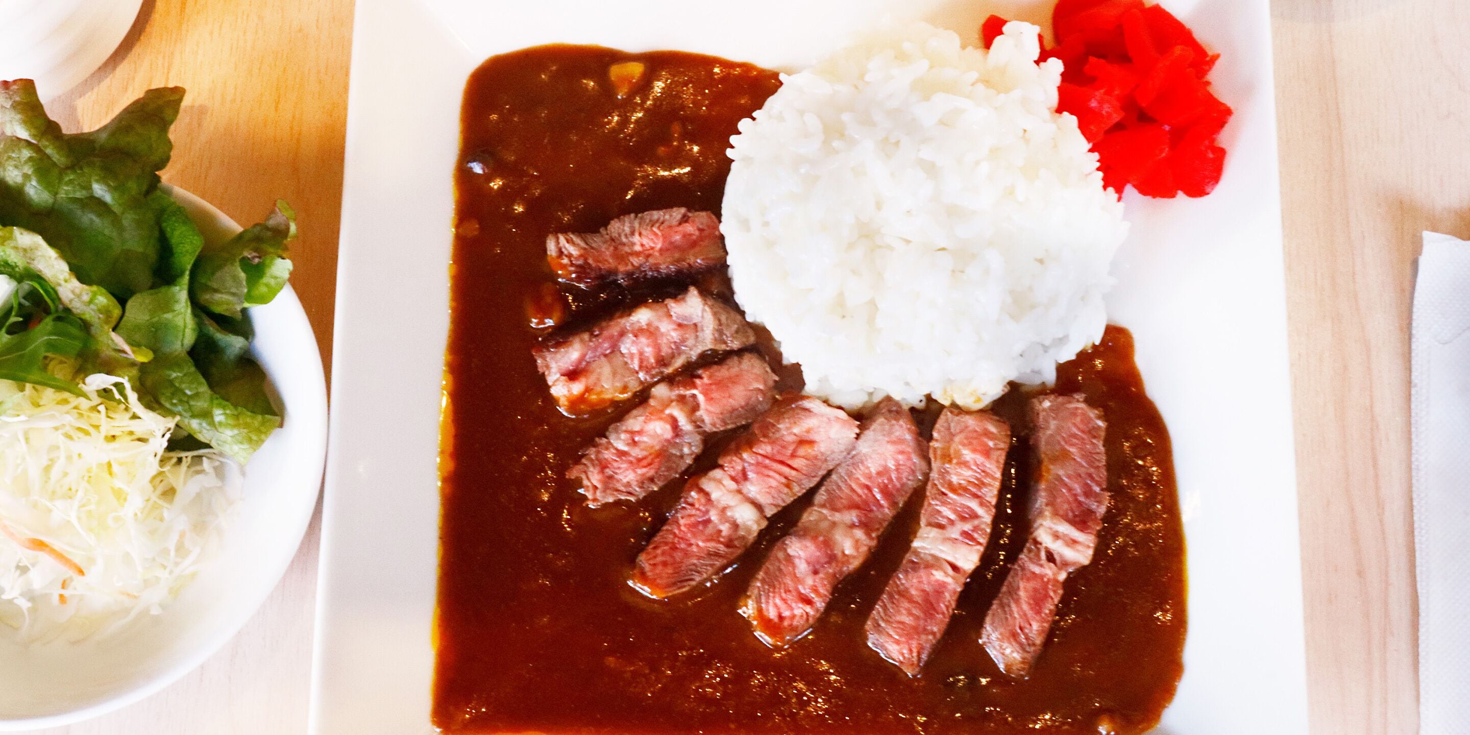 Un plato de carne en rodajas acompañado de arroz y ensalada de col.