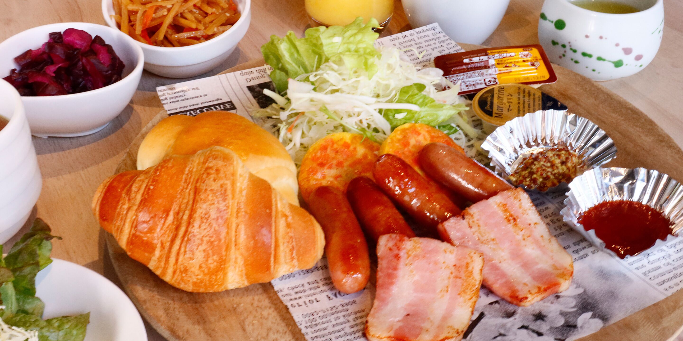 Un plato con salchichas, tocino y un croissant sobre una mesa de madera.