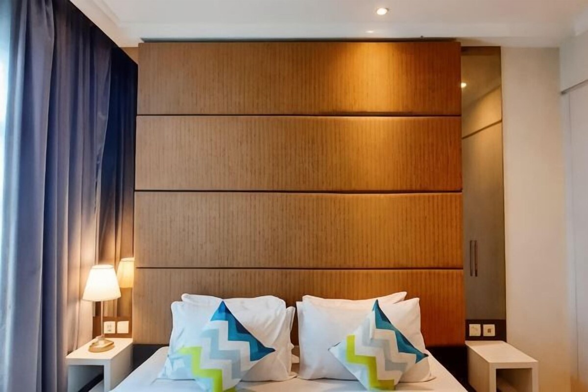 A hotel room with a bed, nightstands, a lamp, and a wooden headboard.