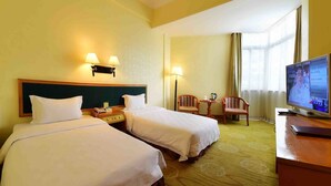 Una habitación de hotel con dos camas, un escritorio, un televisor y una ventana con cortinas.