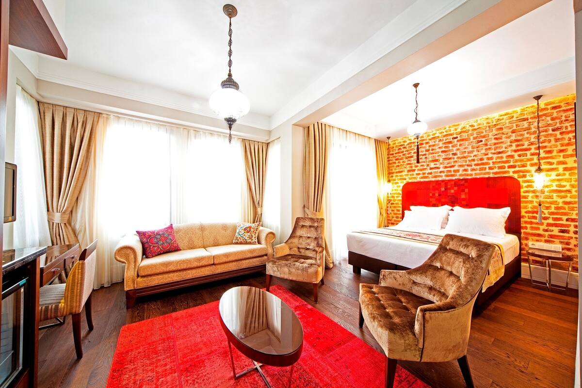 A hotel room with a red carpet, a sofa, a chair, a bed, and a brick-patterned wall.