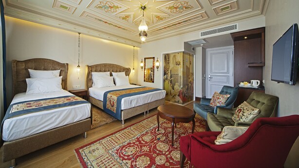 Une chambre d’hôtel avec deux lits, un fauteuil rouge, une petite table et un téléviseur.