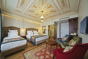 A hotel room with two beds, a red armchair, a small table, and a television. - Azade Suites (Istanbul)