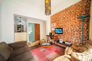 A living room with a brick wall, a television, a desk, and a sofa. - Azade Suites (Istanbul)