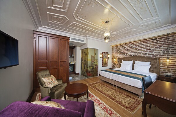 A hotel room with a large bed, a wooden wardrobe, a seating area with a purple sofa, a small round table, and a television mounted on the wall. - Azade Suites (Istanbul)