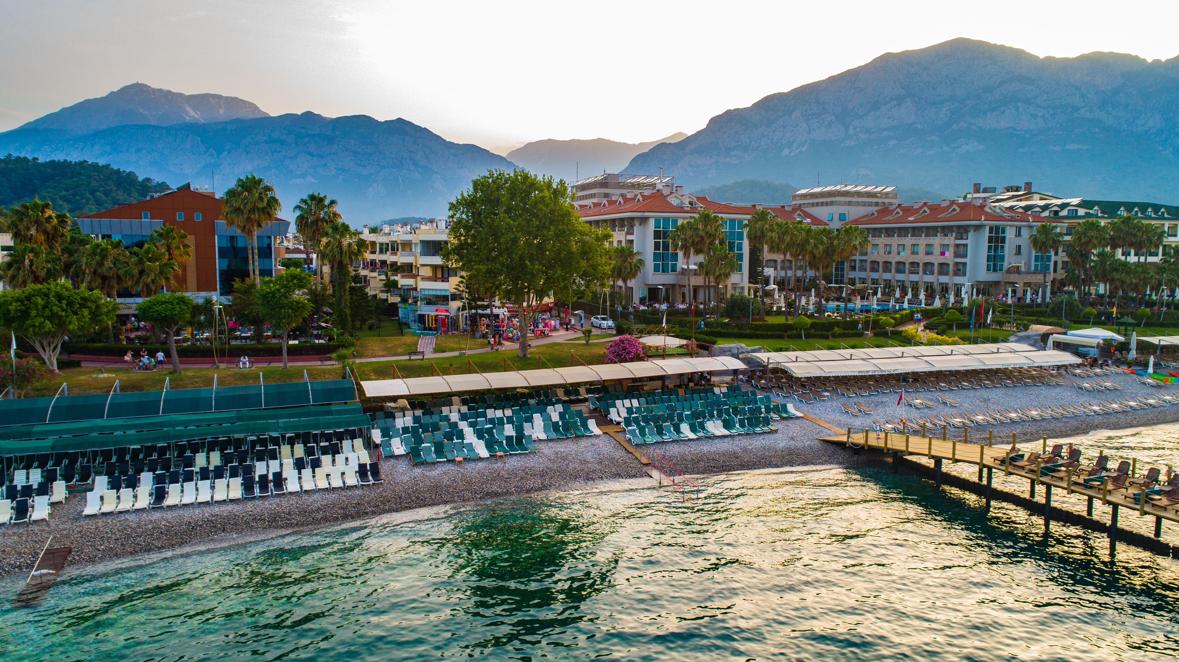 A beachside hotel with rows of sun loungers, a pool area, and mountain views in the background.