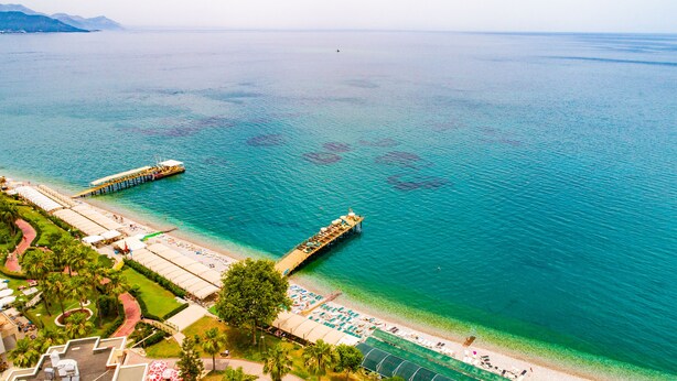 A coastal resort with a pier extending into the sea, a beach area with sun loungers, and a tennis court. - Ambassador Plaza (Kemer)