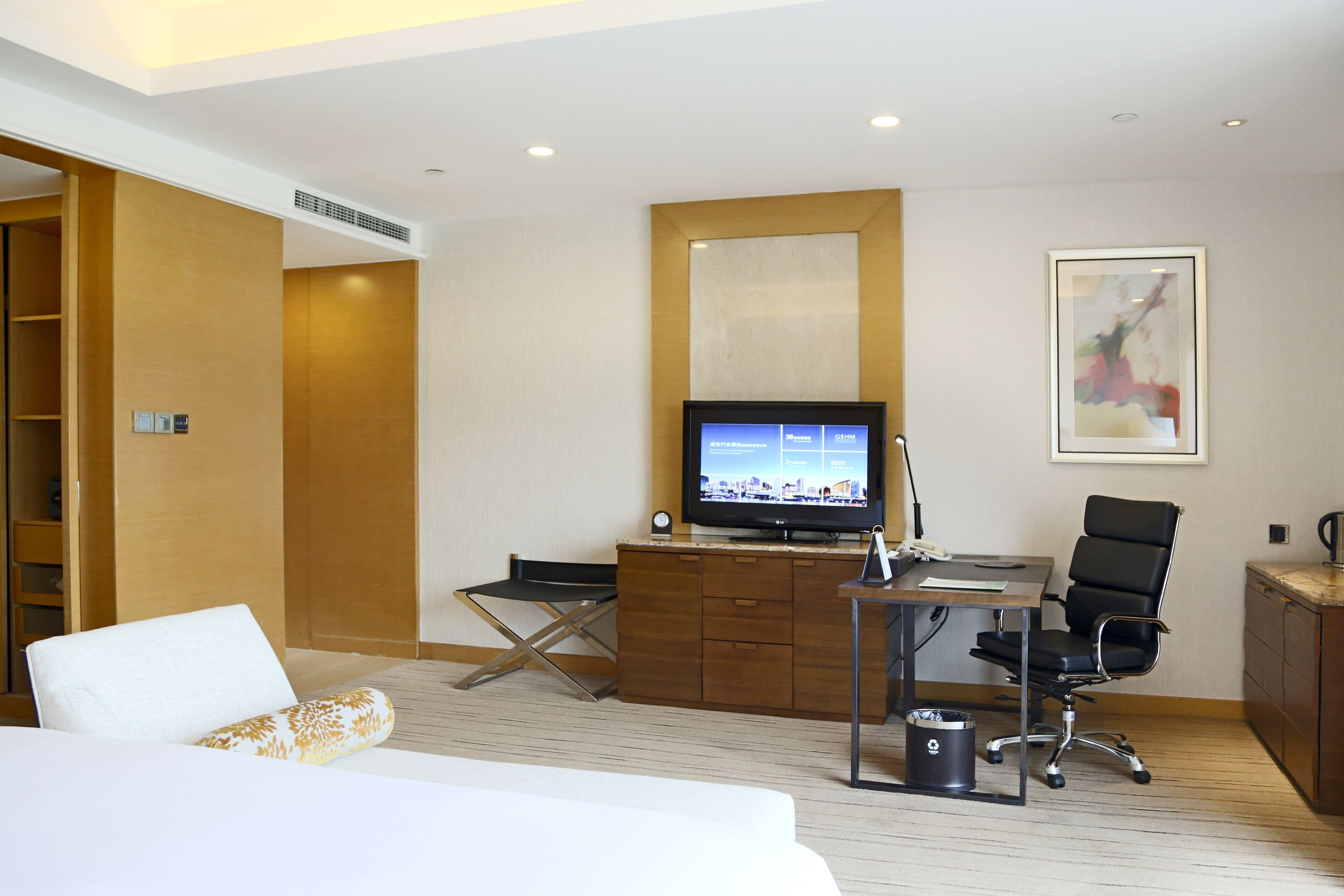 A hotel room with a bed, a desk with a computer, a chair, a TV, and a cabinet.