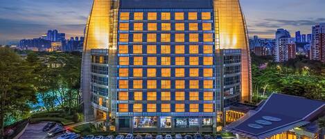 A modern hotel with a prominent entrance, multiple floors, and a parking lot with several cars.