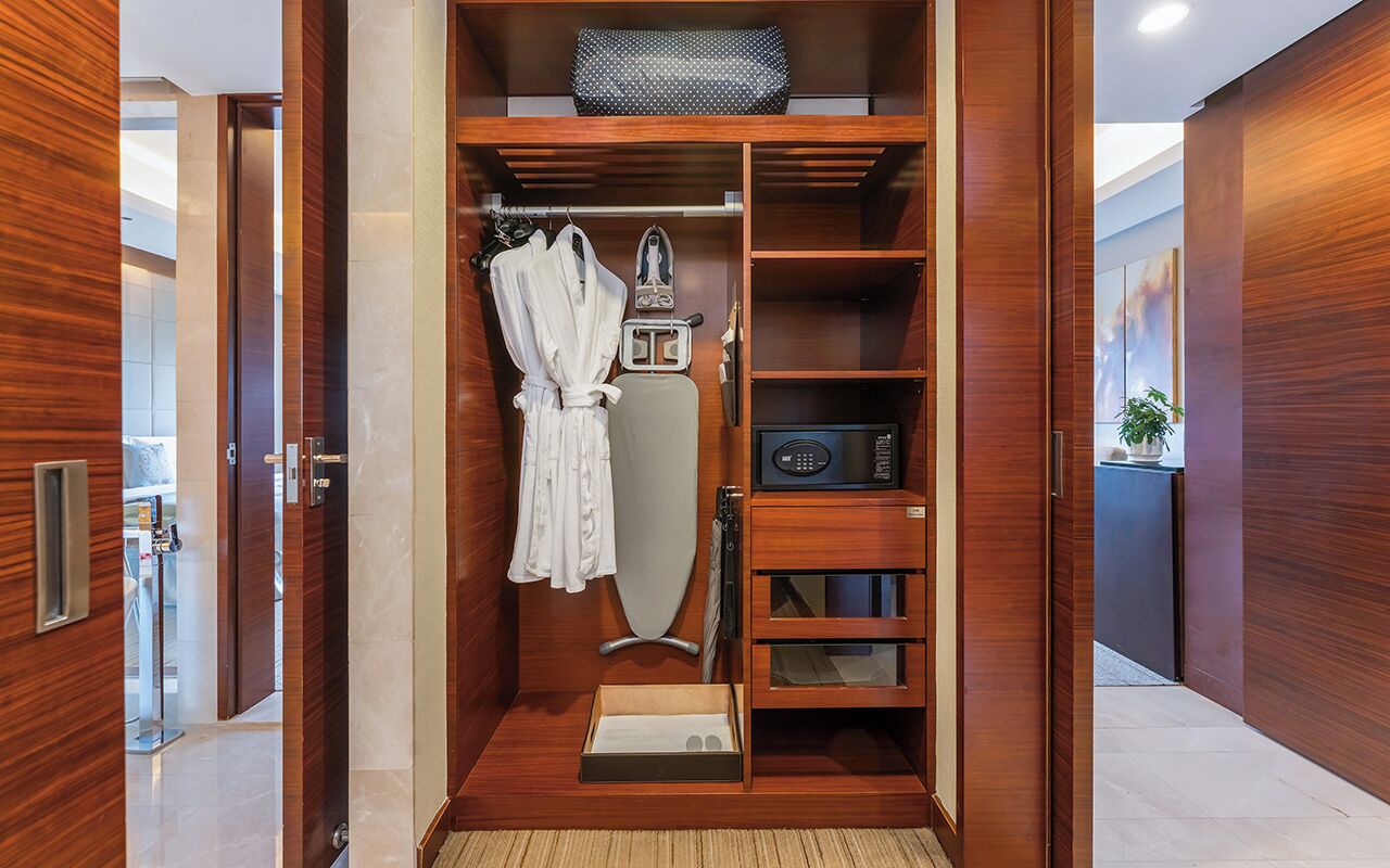 A walk-in closet with wooden paneling, a robe hanging, an ironing board, and a radio.