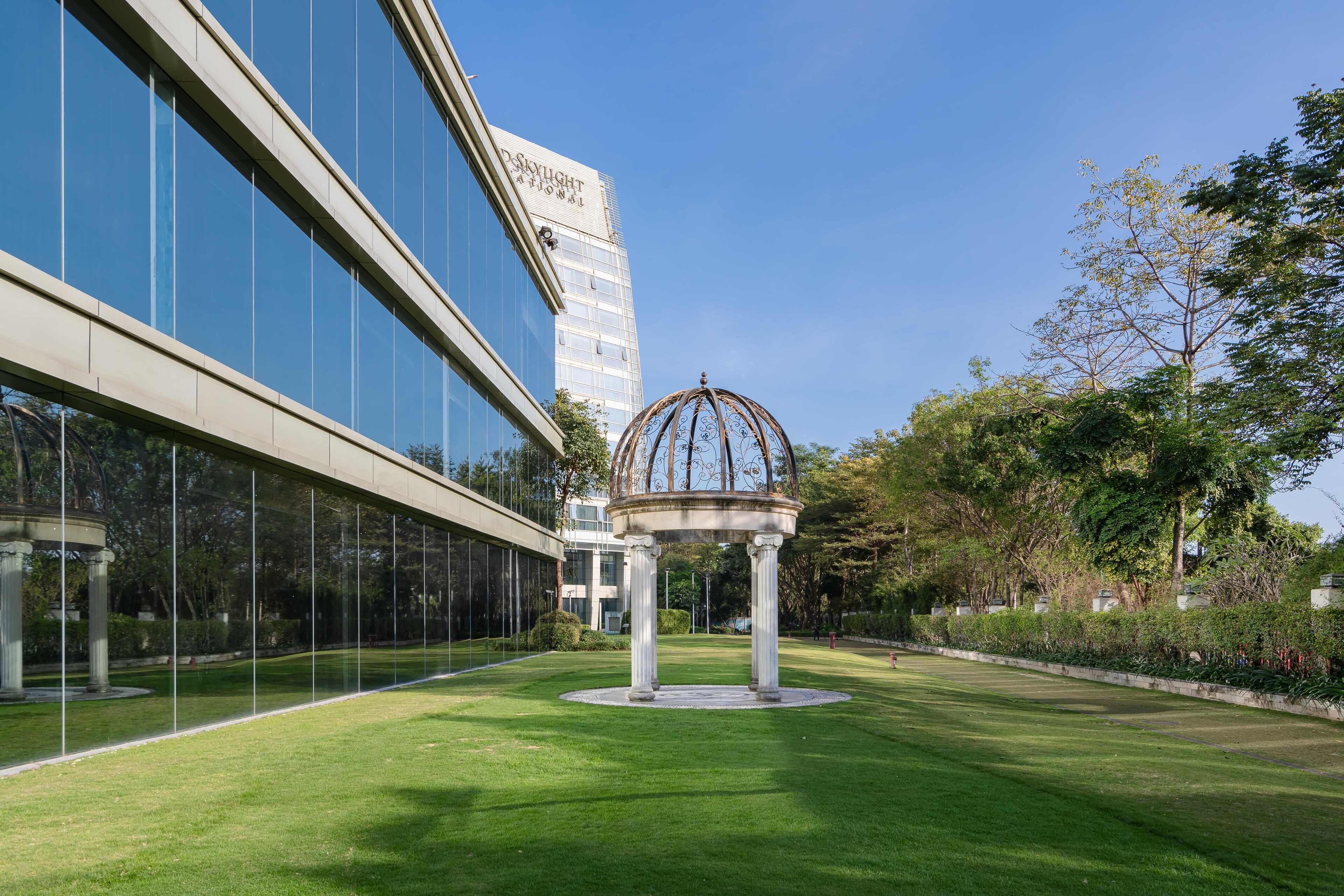 Un edificio moderno con fachada de vidrio y un jardín central con un pabellón.