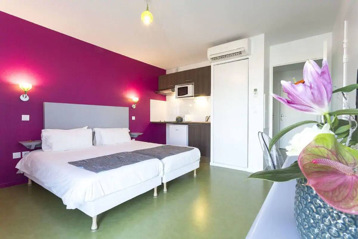 Een slaapkamer met een bed, nachtkastjes, een klein keukenblok en een potplant.