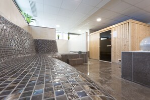 Uma área de spa moderna com um banco revestido de mosaicos, sauna de madeira e chão ladrilhado.