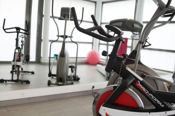 Uma bicicleta ergométrica numa academia, com outros equipamentos de exercícios ao fundo.